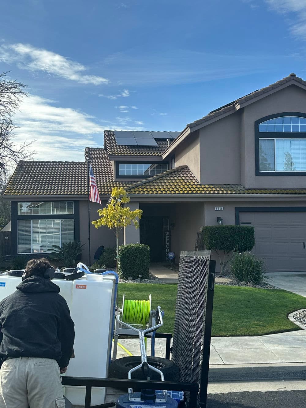 Man preparing equipment outside a suburban home with solar panels and an American flag.