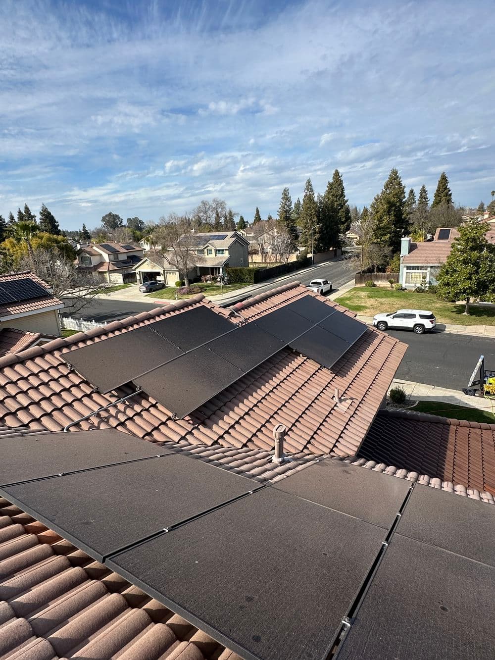 Roof with solar panels, overlooking residential neighborhood and street under a blue sky.
